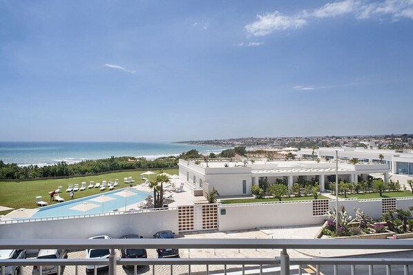 A modern hotel with a pool, lounge chairs, and a view of the ocean.
