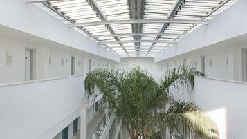 A multi-level atrium with glass railings, a central palm tree, and modern white furnishings.
