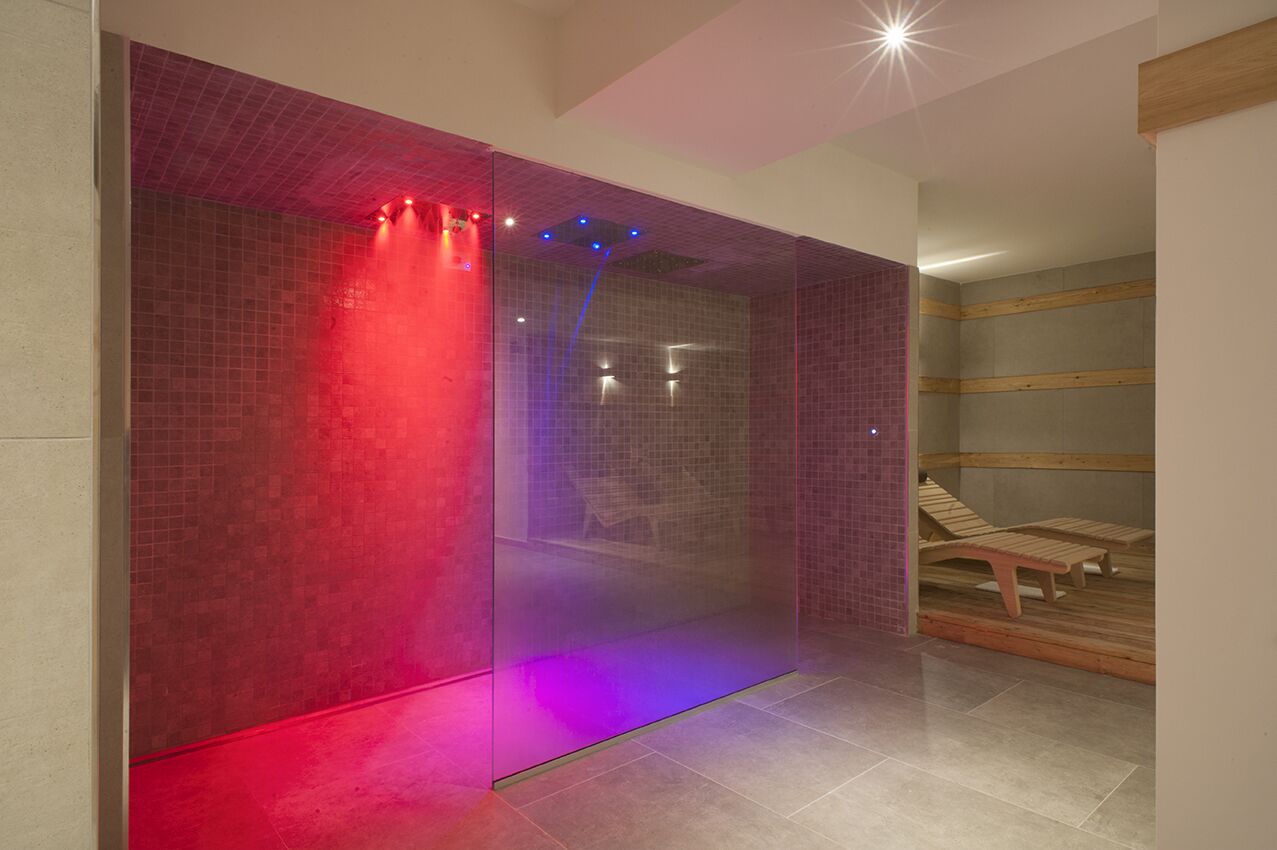 Une salle de spa moderne dotée d’une paroi en verre, d’un plancher chauffant et de chaises longues en bois.