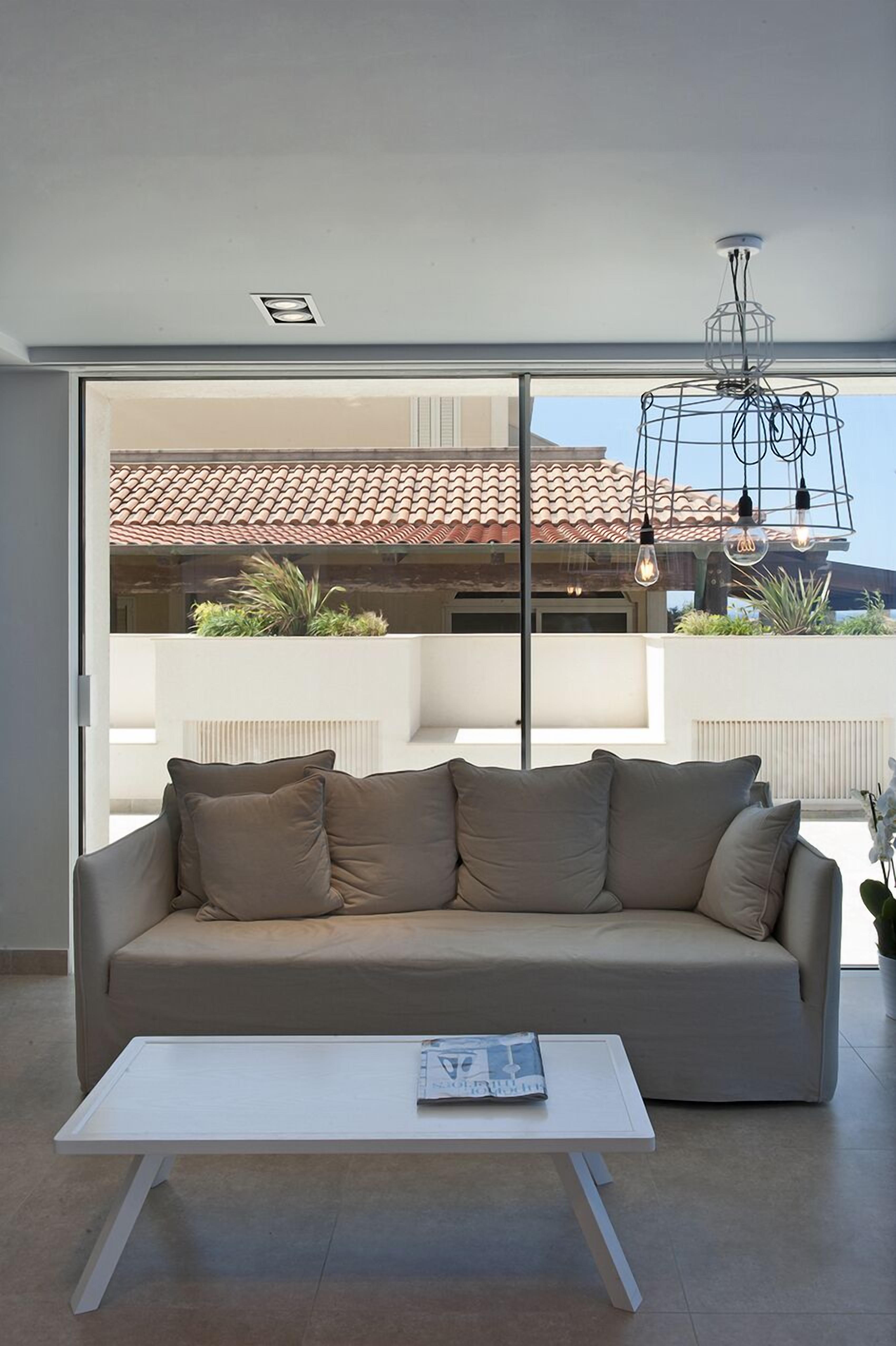 A modern living room with a beige sofa, a white coffee table, and a large window offering a view of a house with a tiled roof.