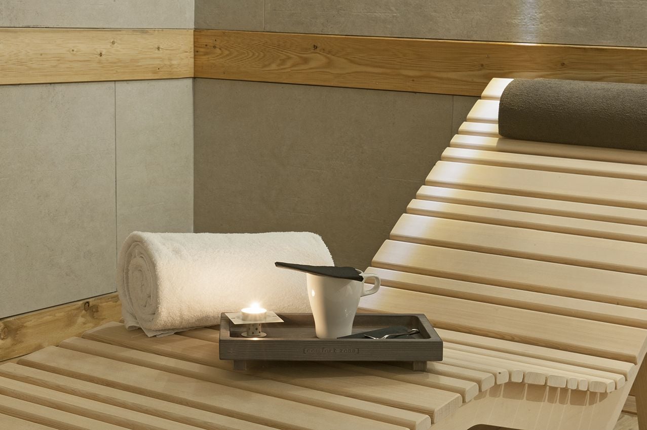Un banc en bois avec une serviette et une tasse posés sur un plateau, une bougie et un panneau en bois accroché au mur.