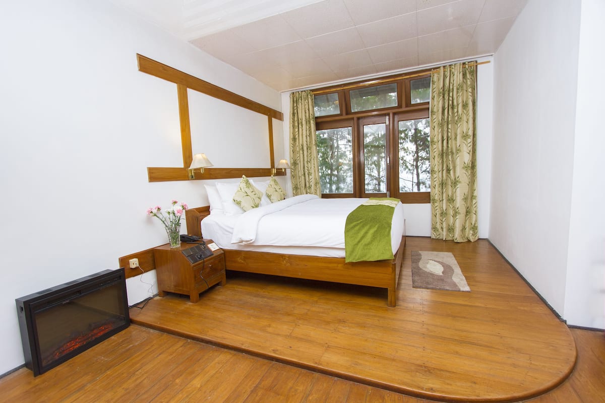 A bedroom with a wooden bed, a nightstand, a TV, and a window with curtains.
