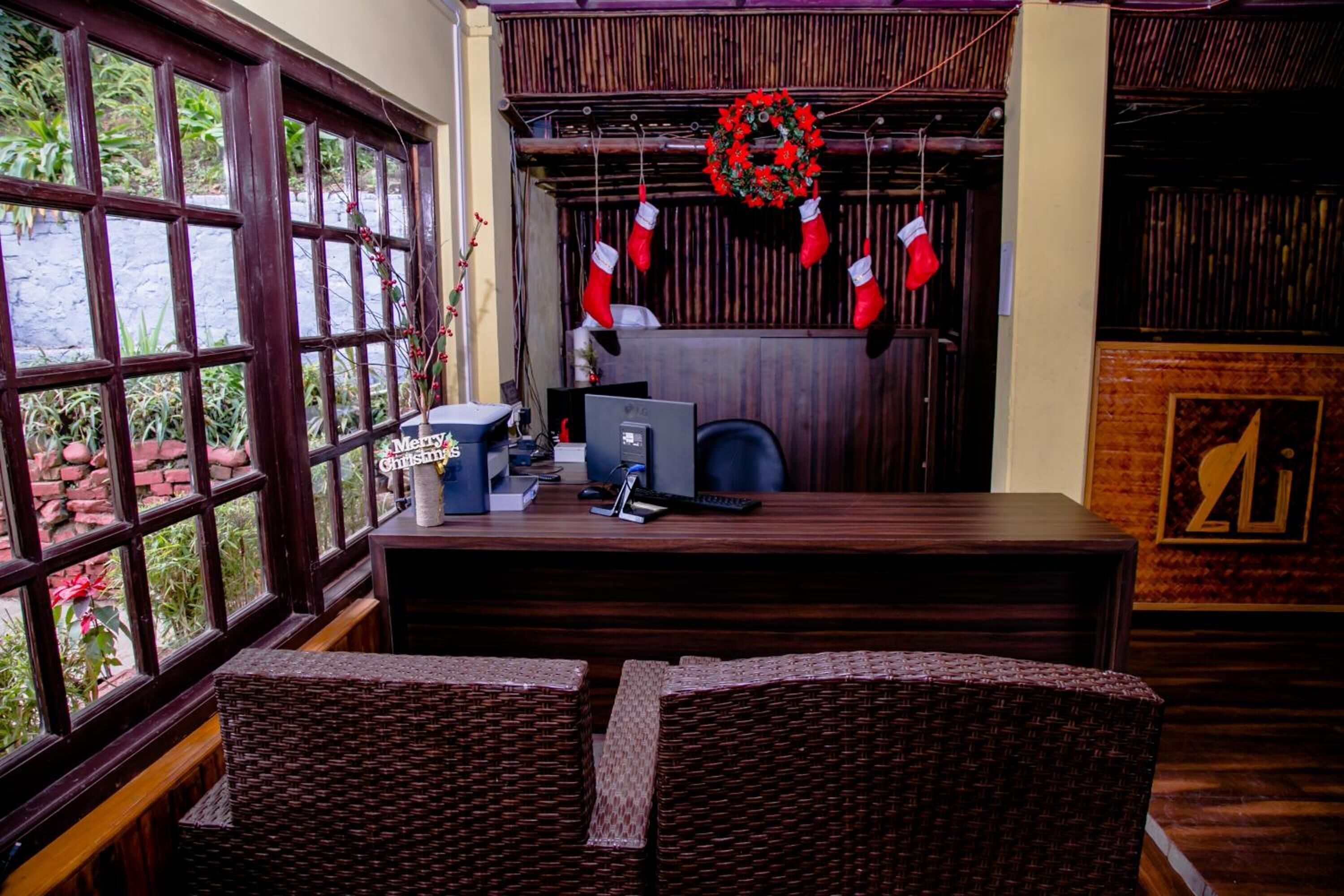 Een receptiezone met een balie, computer en rieten stoelen. Een kerstkrans hangt boven de balie.