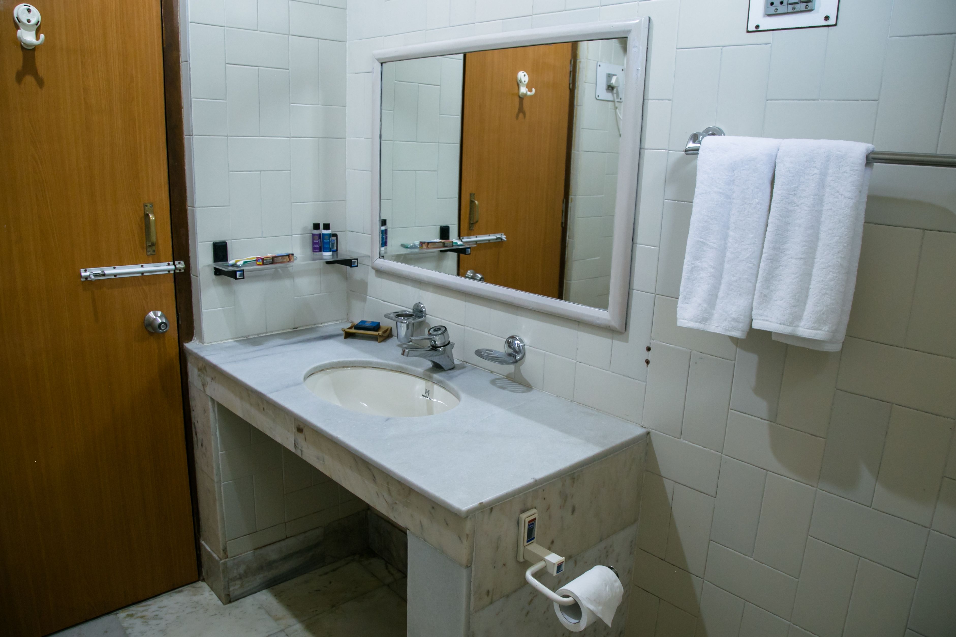 Un baño con lavamanos, espejo, toallero y dispensador de papel higiénico.
