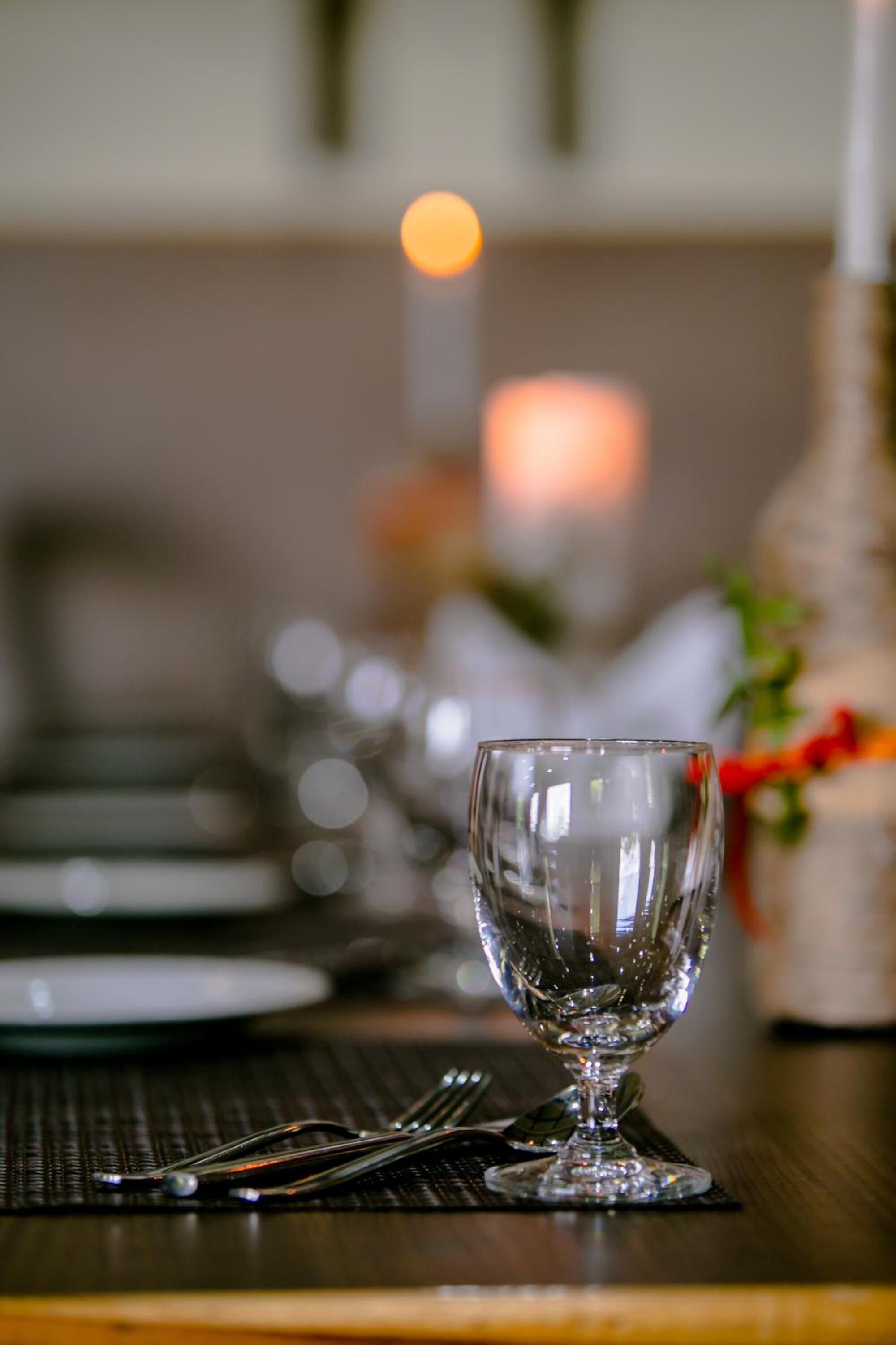A dining table set with a clear glass wine glass, cutlery, and plates.
