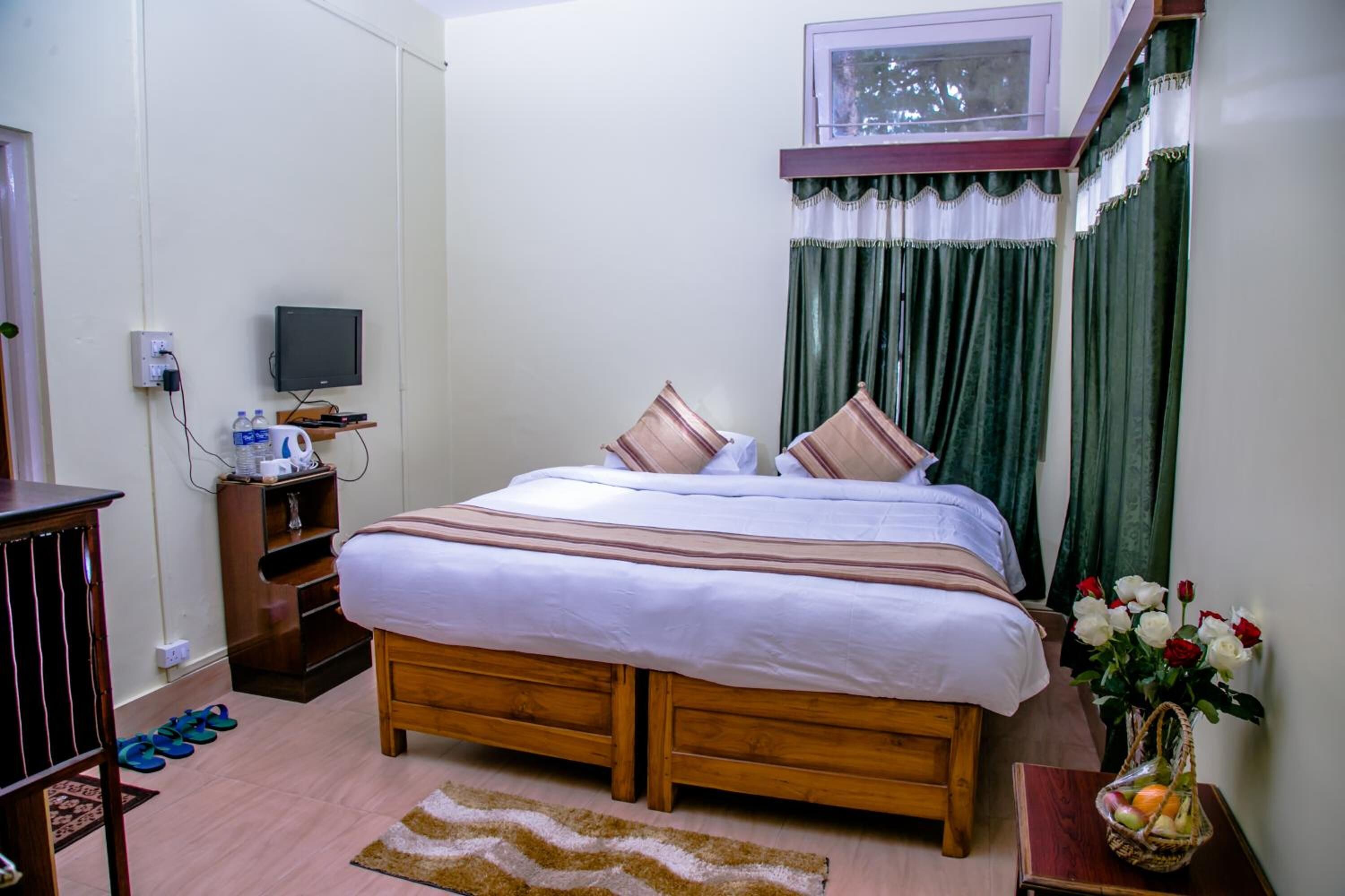 Ein ordentlich eingerichtetes Schlafzimmer mit einem Holzbett, einem Fernseher auf einem Regal, einem kleinen Schreibtisch und einem Fenster mit Vorhängen.