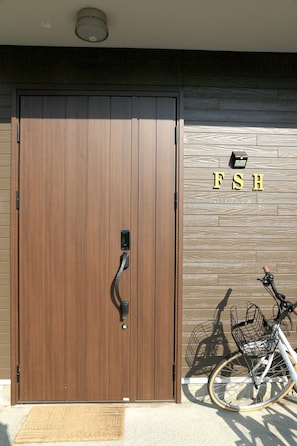 Uma porta dupla de madeira com maçaneta, um suporte para bicicletas e uma placa com a inscrição 'FSH'.