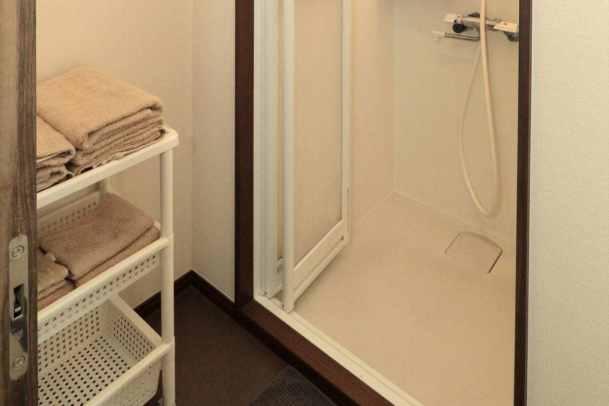 A shower with a white door, a shelf with toiletries, and a towel rack.