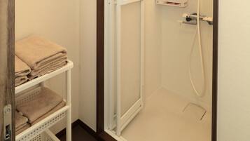 A shower with a white door, a shelf with toiletries, and a towel rack.