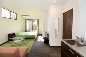 Quarto de hotel com cama, mesa de vidro, sofá, cozinha com pia e uma janela grande.