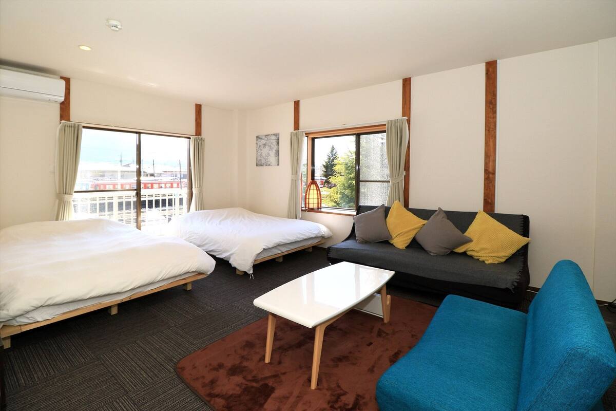 A hotel room with two beds, a sofa, a coffee table, and large windows with curtains.
