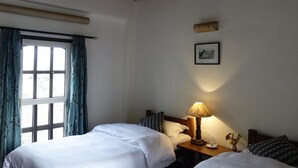 Una camera con due letti, un comodino con lampada, una finestra con tende e un quadro appeso al muro.