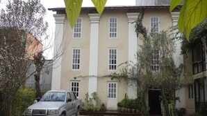Un edificio con un ingresso centrale, un veicolo parcheggiato e vegetazione circostante.