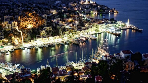 Une ville côtière de nuit, avec des bâtiments illuminés, un port de plaisance et des bateaux.