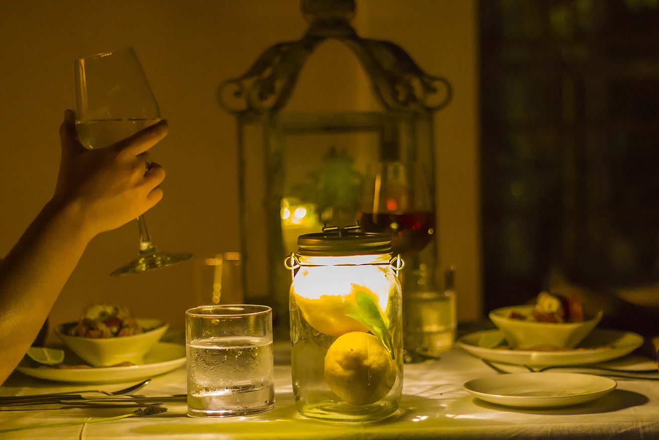 A dining table with a glass of water, a glass of wine, a jar with a lemon, and a candle in the background.