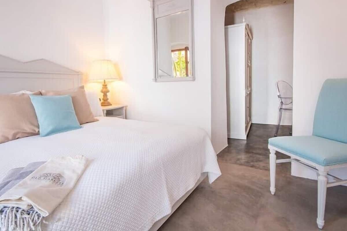 A bedroom with a bed, a chair, a nightstand with a lamp, and a mirror.