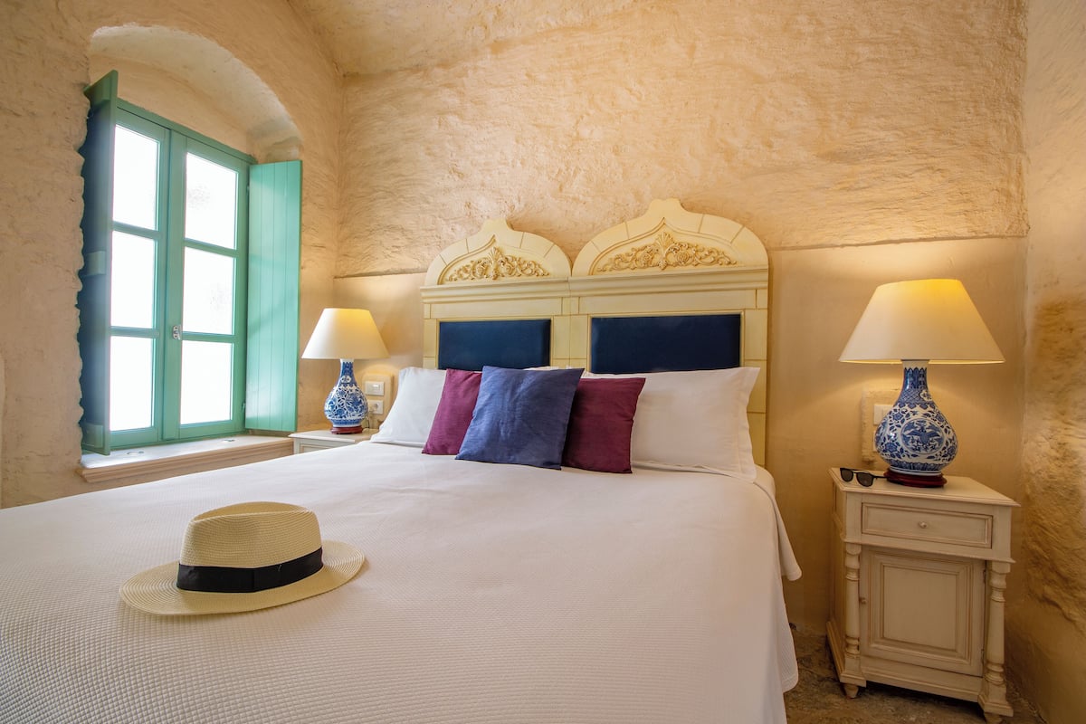 A bedroom with a large bed, a window with green shutters, and two bedside lamps.