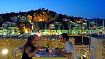 A couple dining at an outdoor table with a view of a hillside town at night.