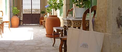 Un espacio de estar al aire libre con mobiliario de madera, macetas de terracota y una bolsa de tela blanca con un logotipo.