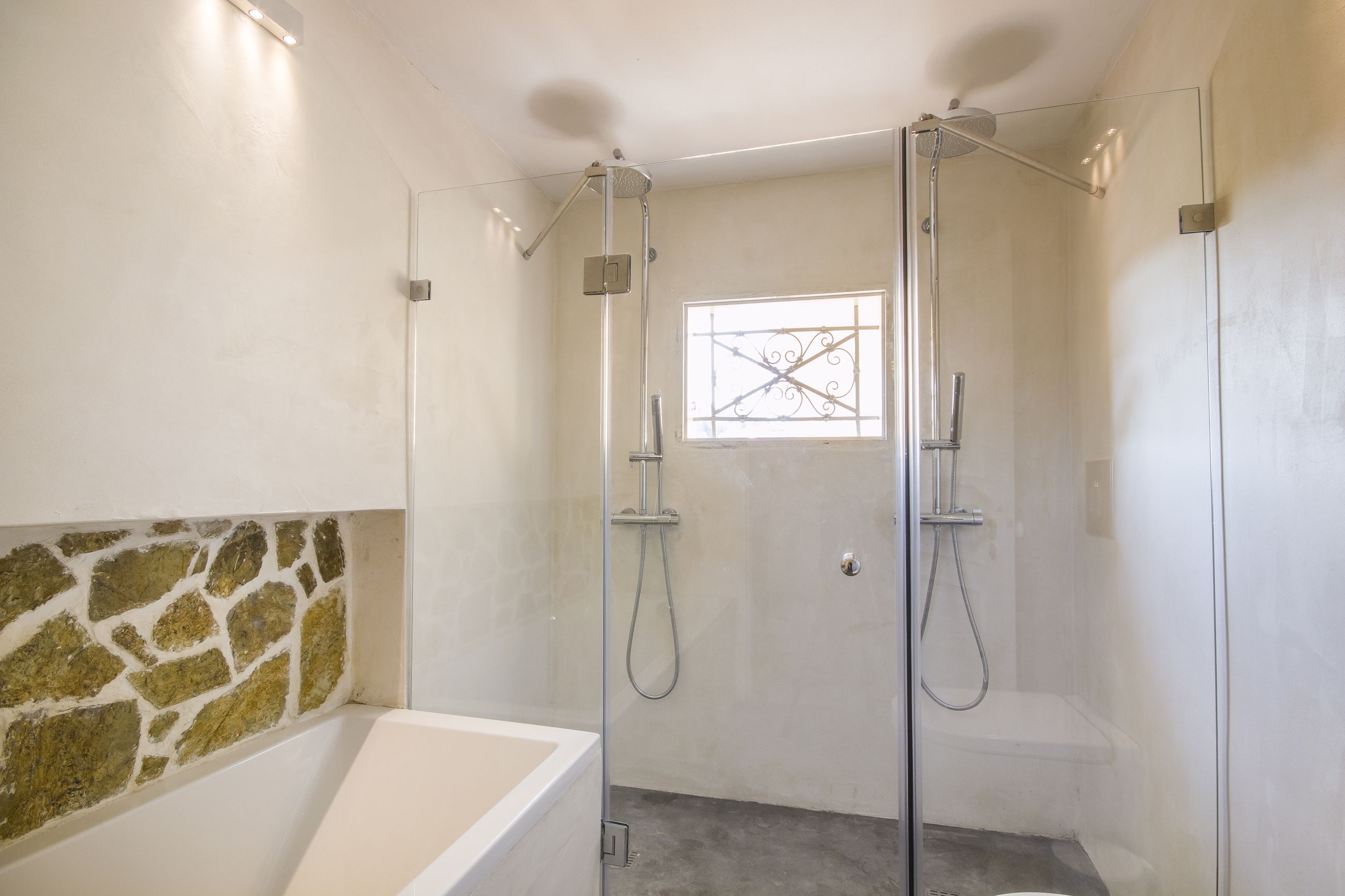 A modern bathroom with a glass-enclosed shower, a bathtub, and a stone accent wall.