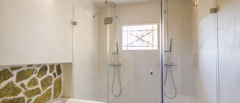 A modern bathroom with a glass-enclosed shower, a bathtub, and a stone accent wall.