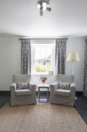 A room with two armchairs, a small table with a vase, and a lamp.