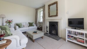 A living room with a white sofa, a coffee table, a fireplace, a television, and a bookshelf. - GARDEN COTTAGE  - peaceful rural cottage in Scottish countryside (Denholm)