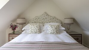 A bedroom with a sloped ceiling, a bed with white bedding and patterned pillows, two bedside lamps, and a nightstand with a vase of flowers. - GARDEN COTTAGE  - peaceful rural cottage in Scottish countryside (Denholm)