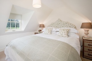 A bedroom with a large bed, two bedside tables, a window, and a sloped ceiling.