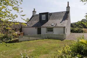 A two-story house with a stone wall, a wooden fence, and a grassy yard.