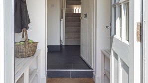 A hallway leading to a staircase with a basket of apples on a table and a coat hanging on the wall. - GARDEN COTTAGE  - peaceful rural cottage in Scottish countryside (Denholm)