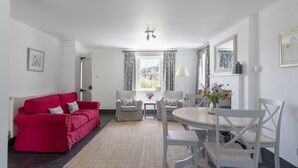 A well-lit room with a red sofa, two armchairs, a dining table with chairs, and a window with curtains. - GARDEN COTTAGE  - peaceful rural cottage in Scottish countryside (Denholm)