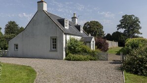 A white house with a steeply pitched roof, a chimney, and a gravel driveway. - GARDEN COTTAGE  - peaceful rural cottage in Scottish countryside (Denholm)