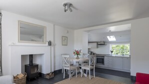 A modern kitchen with white cabinets, a dining area with a round table and chairs, a fireplace, and a red sofa. - GARDEN COTTAGE  - peaceful rural cottage in Scottish countryside (Denholm)