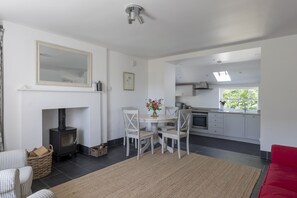 A modern kitchen with white cabinets, a dining area with a round table and chairs, a fireplace, and a red sofa. - GARDEN COTTAGE  - peaceful rural cottage in Scottish countryside (Denholm)