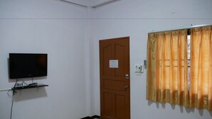 Una habitación con una cama, televisión montada en la pared, una puerta y una ventana con cortinas.