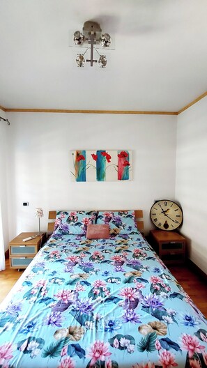 A bedroom with a floral bedspread, a wall clock, and a ceiling fan.