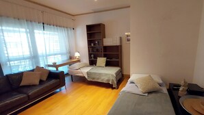 A compact room with two single beds, a sofa, a bookshelf, and a small table with a lamp.