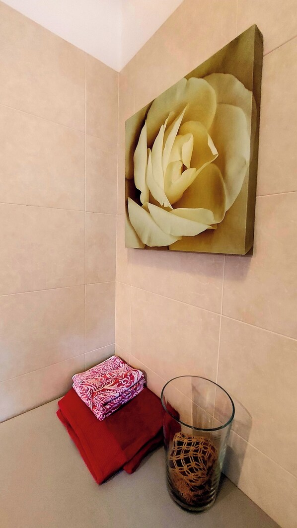 A bathroom with beige tiles, a large floral painting, a glass vase with a net, and a red towel.