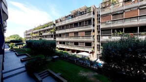 A multi-story building with balconies, some with plants. There are steps leading to the entrance.