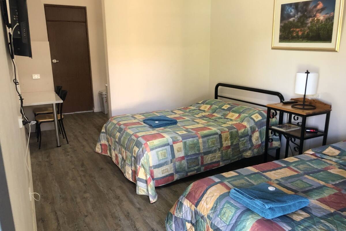 Ein Zimmer mit zwei Betten, einem Schreibtisch, einem Stuhl und einer Tür.