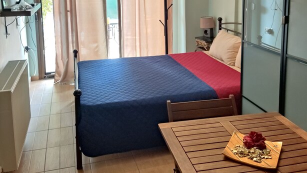 Ein Schlafzimmer mit Bett, Tisch mit Dekoration, Kleiderständer und Blick ins Freie.