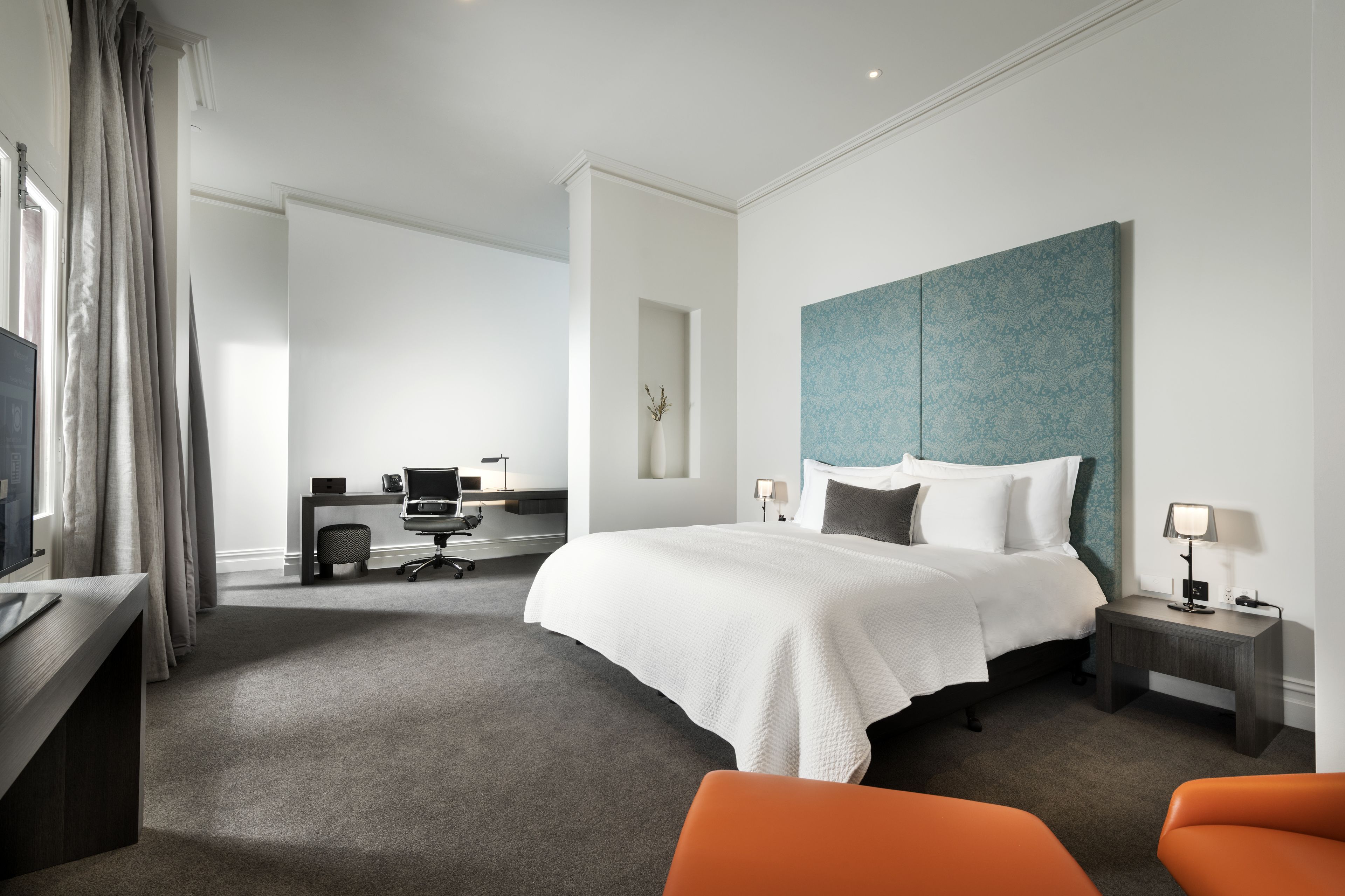 Una habitación de hotel moderna con una cama grande, un escritorio con computadora, una silla y un televisor.