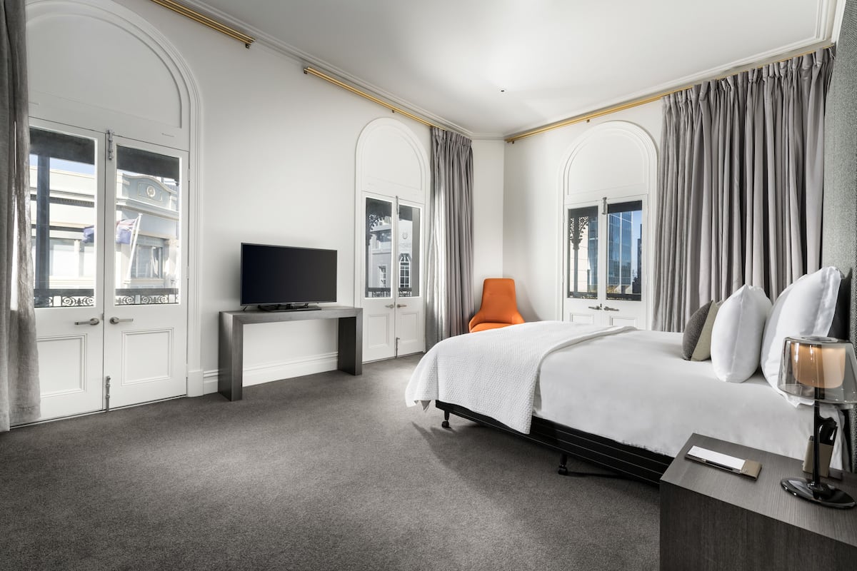 A hotel room with a large bed, a desk with a flat-screen TV, and a chair.