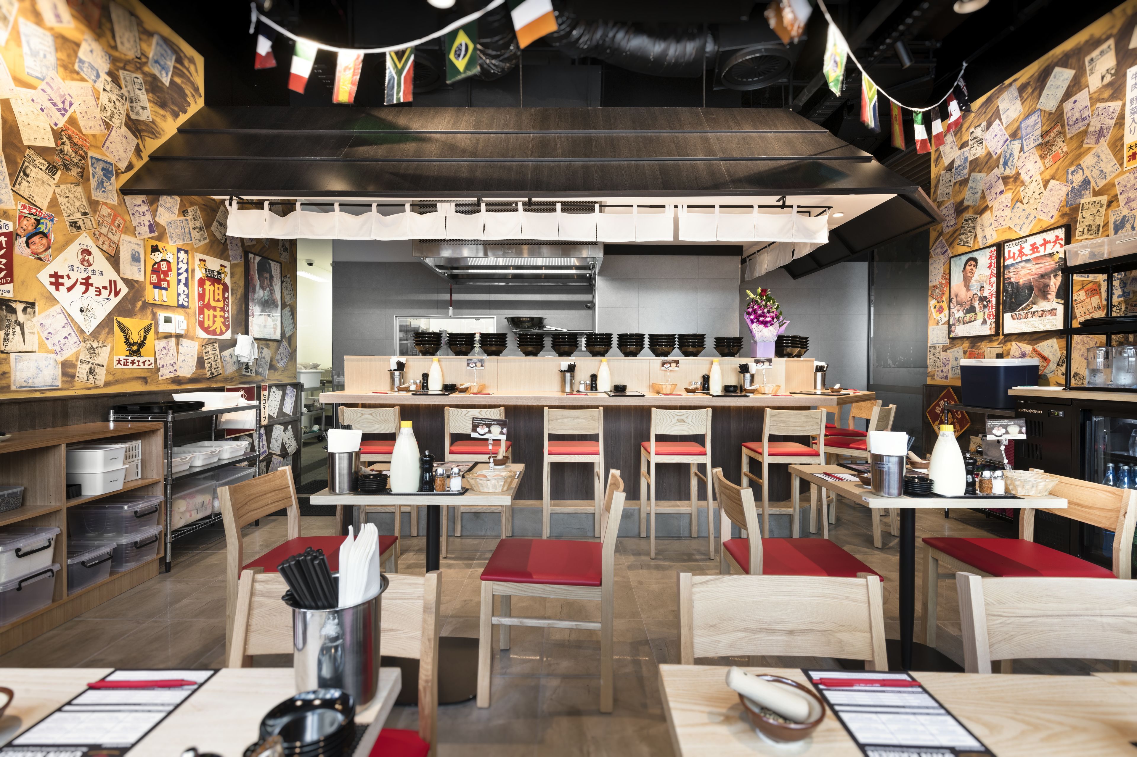 A restaurant interior with wooden tables, red cushioned chairs, and a kitchen area with stainless steel appliances.