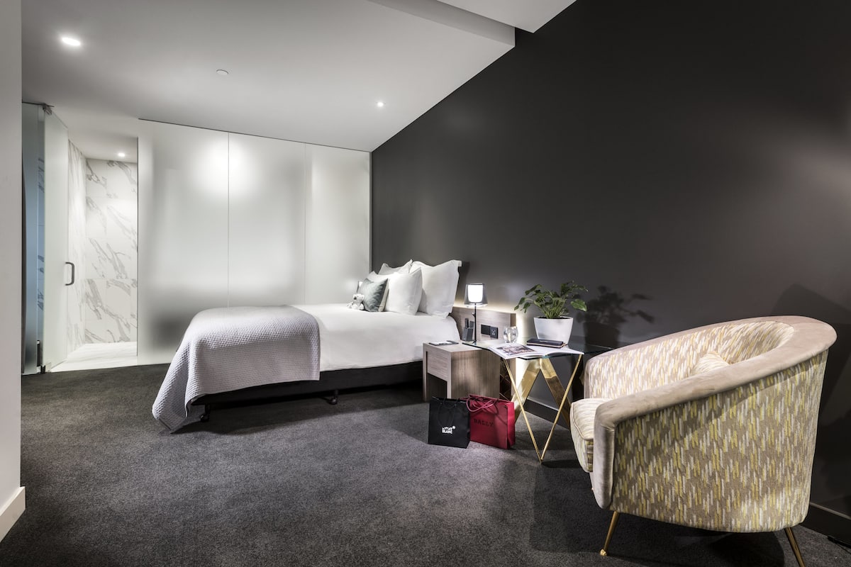 A modern bedroom with a bed, bedside table, lamp, chair, and a dark accent wall.