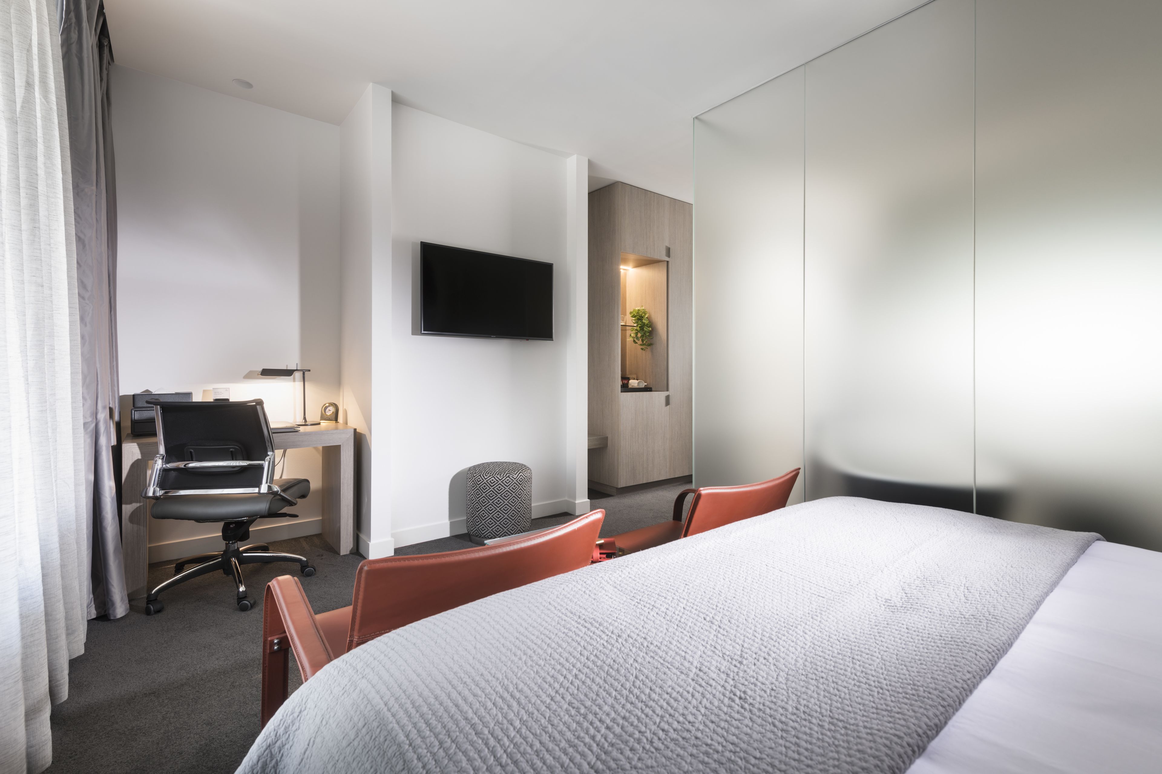 A hotel room with a bed, a desk with a computer, a TV mounted on the wall, and a small seating area with chairs.