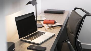 A laptop on a desk with a lamp, glasses, a cup, and a notebook.
