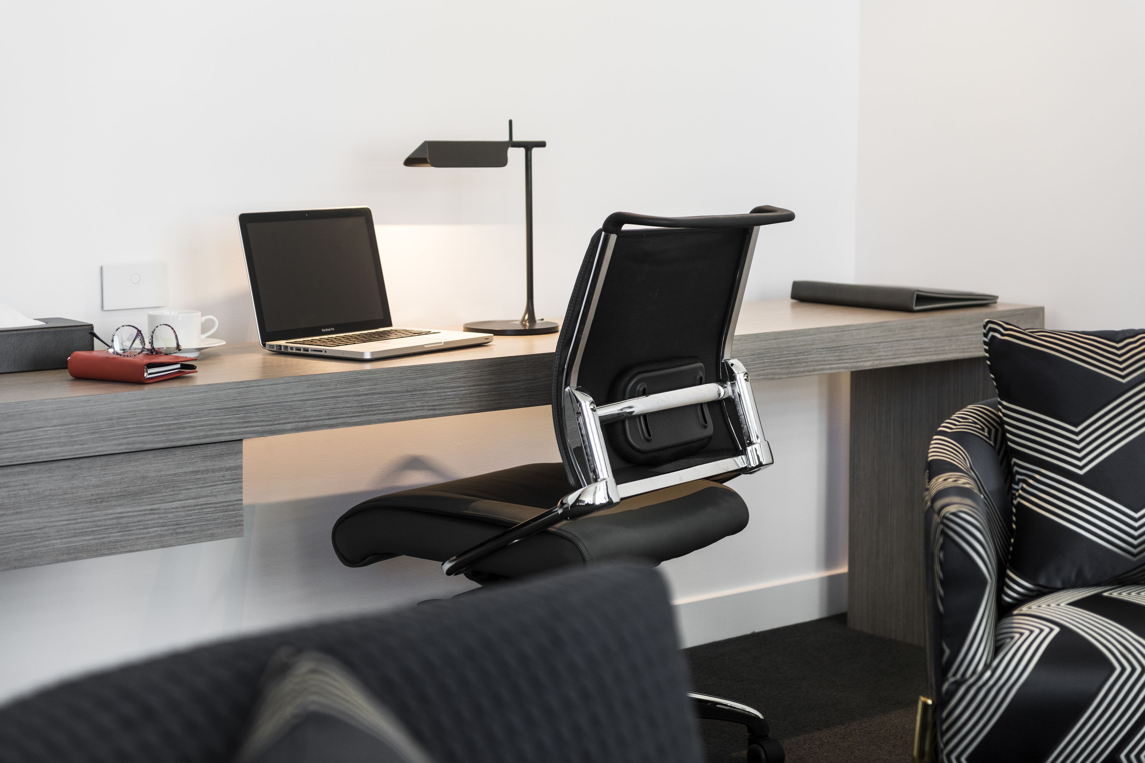 Ein moderner Arbeitsplatz mit einem Laptop, einer Schreibtischlampe und einem Stuhl mit Metallgestell.