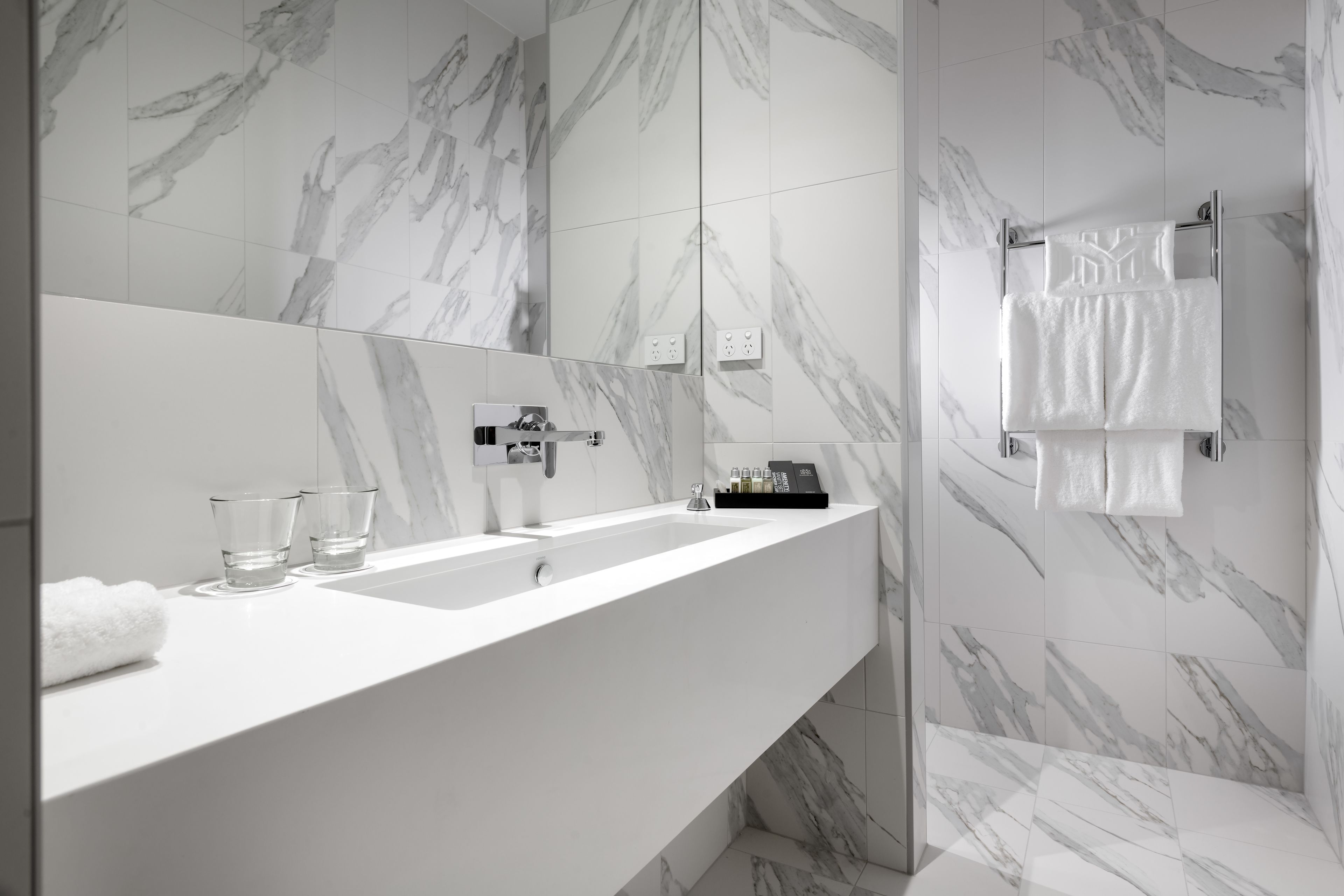 Een moderne badkamer met een grote spiegel, een wit wastafelmeubel en een handdoekrek.